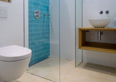 Badkamer met turquoise keramische wandtegels, travertine beige vloertegels, inbouwtoilet en waskom